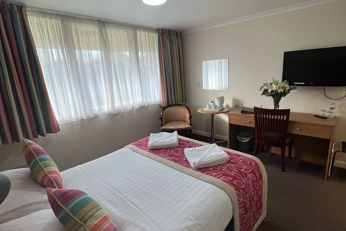 Habitación de hotel con dos camas, un escritorio, una silla, un televisor y una ventana con cortinas.