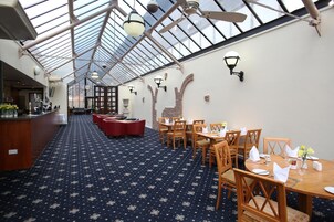 Un restaurante con techo alto y tragaluces, mesas y sillas de madera, y una alfombra estampada.