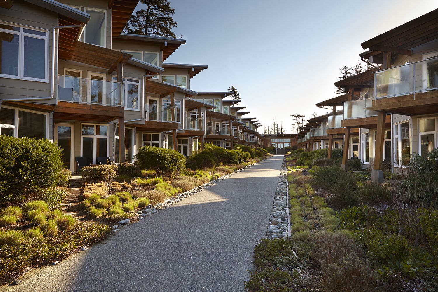 A row of modern, multi-story residential buildings with balconies, a gravel pathway, and landscaped greenery.