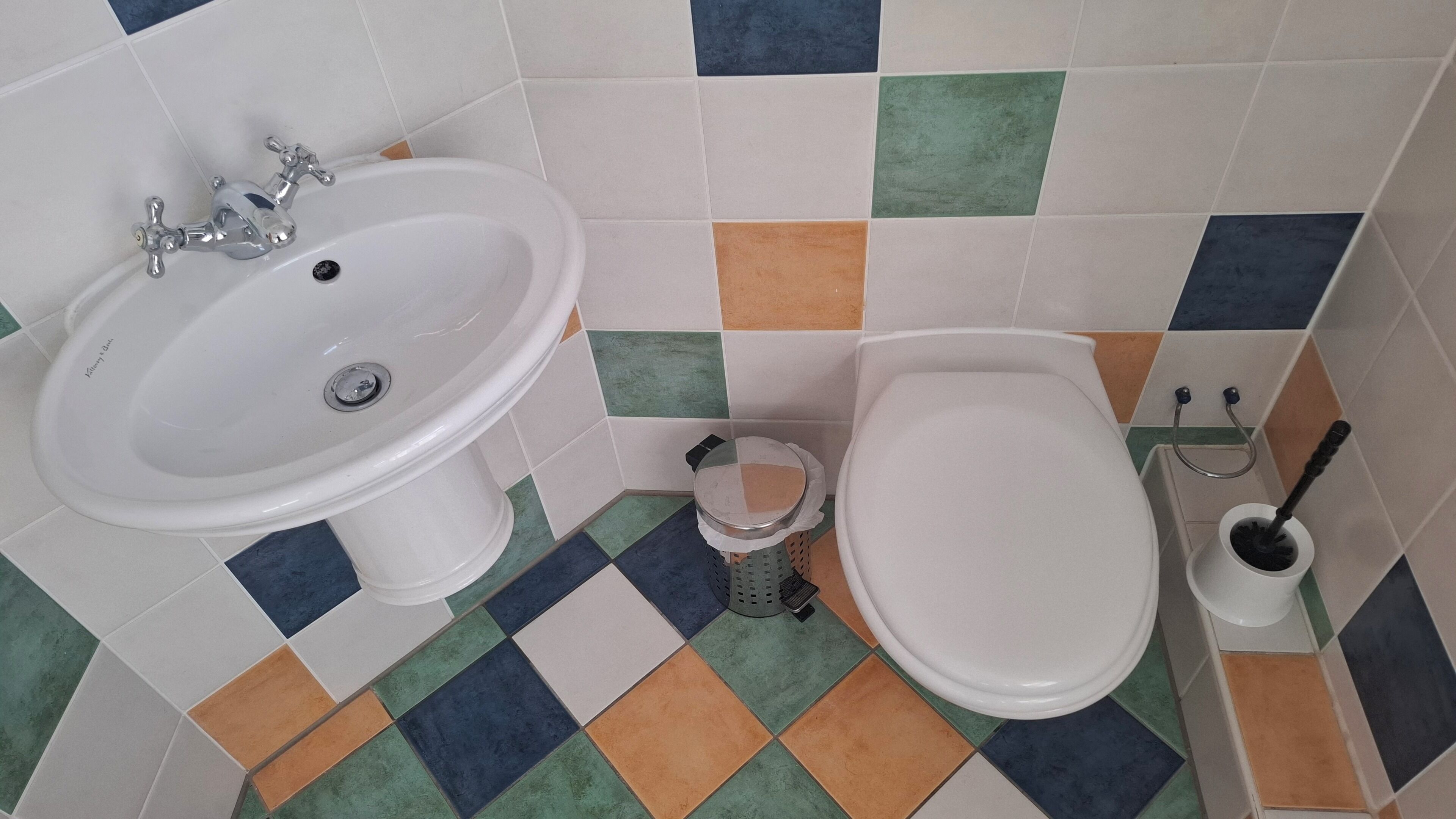 Et badeværelse med en hvid vask, toilet og bidet. Gulvet har et skakmønster.