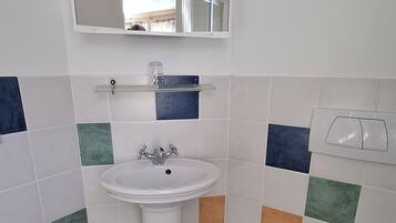 A bathroom with a white sink, a mirror above it, and a toilet. The floor has a checkered tile pattern.