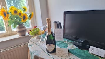 A table with a bottle of champagne, a vase of sunflowers, a fruit bowl, and a sign welcoming guests.