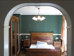 A bedroom with a wooden bed, green polka dot wallpaper, a nightstand with a lamp, and a window with curtains.