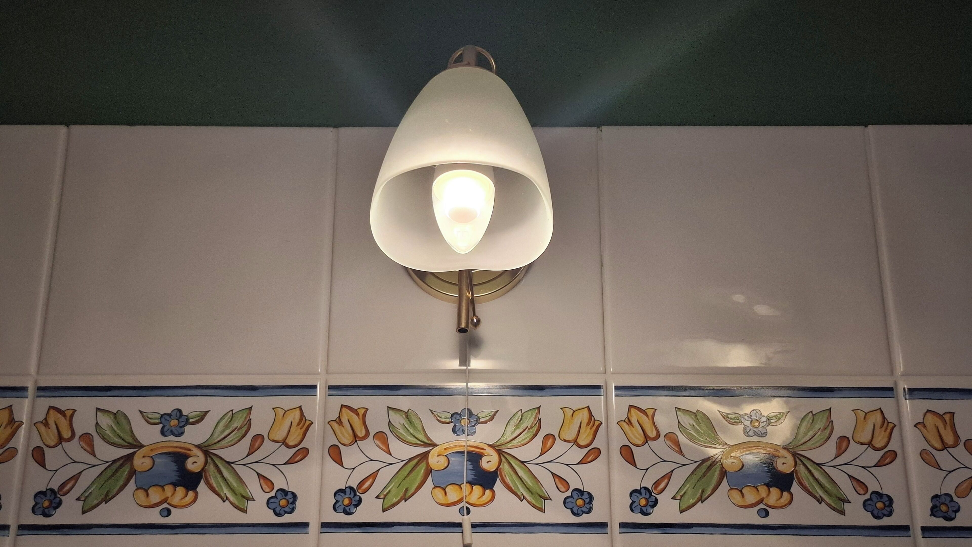 A wall with a decorative tile pattern and a wall-mounted light fixture.