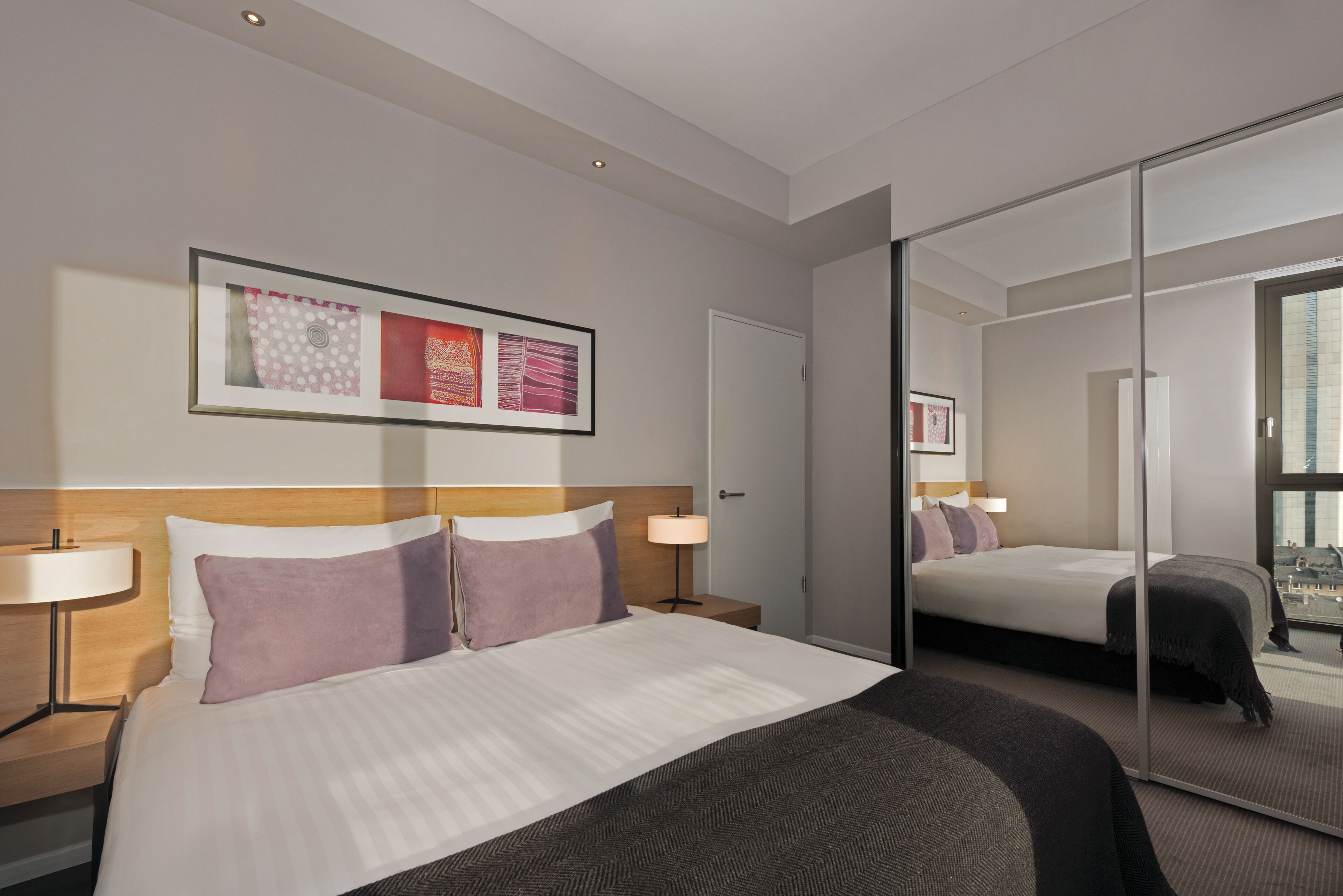 A hotel room with a bed, bedside tables, a mirror, and a framed artwork on the wall.