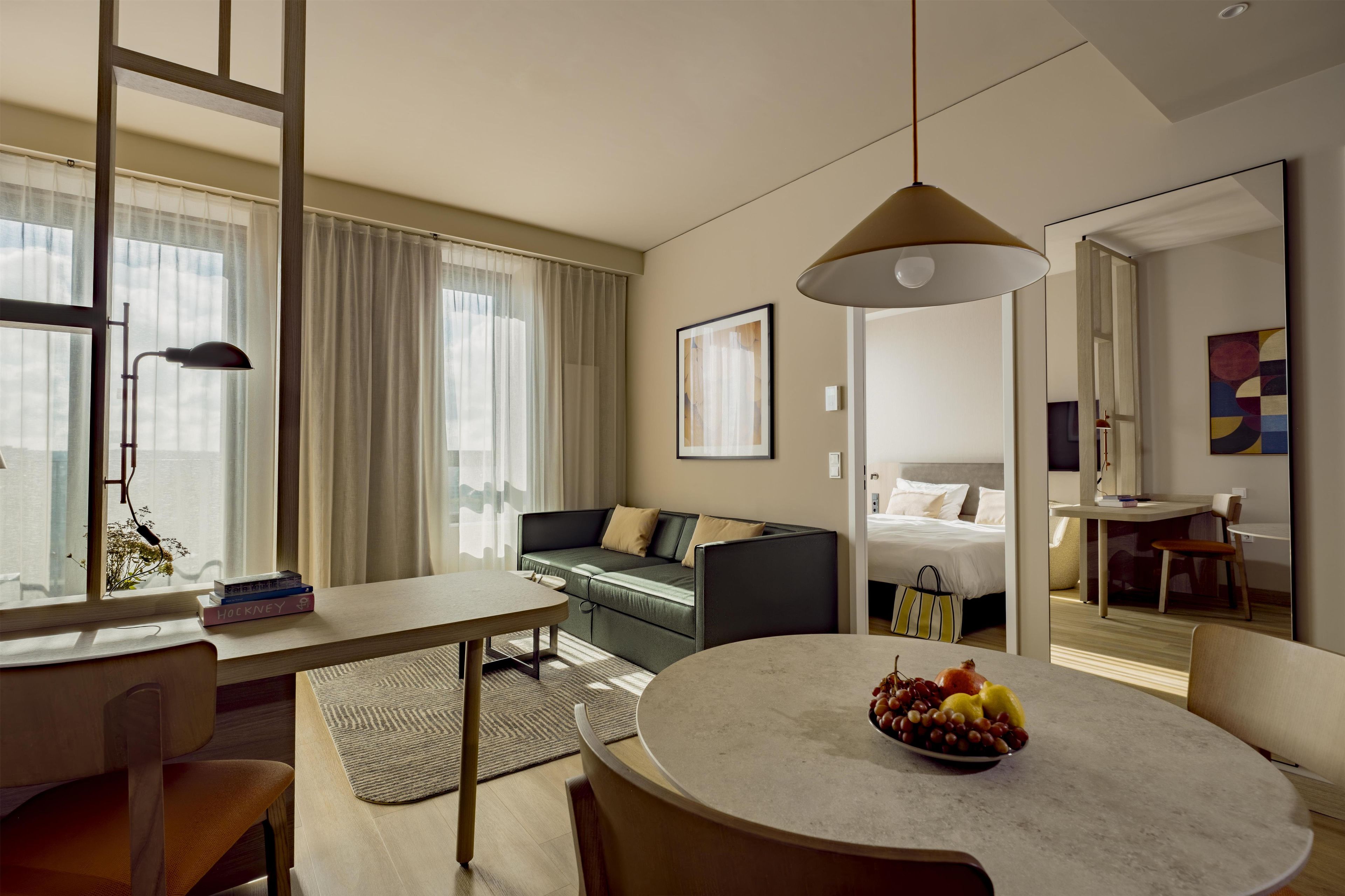 A modern hotel room with a dining area, a sofa, a bed, and a view of the city.