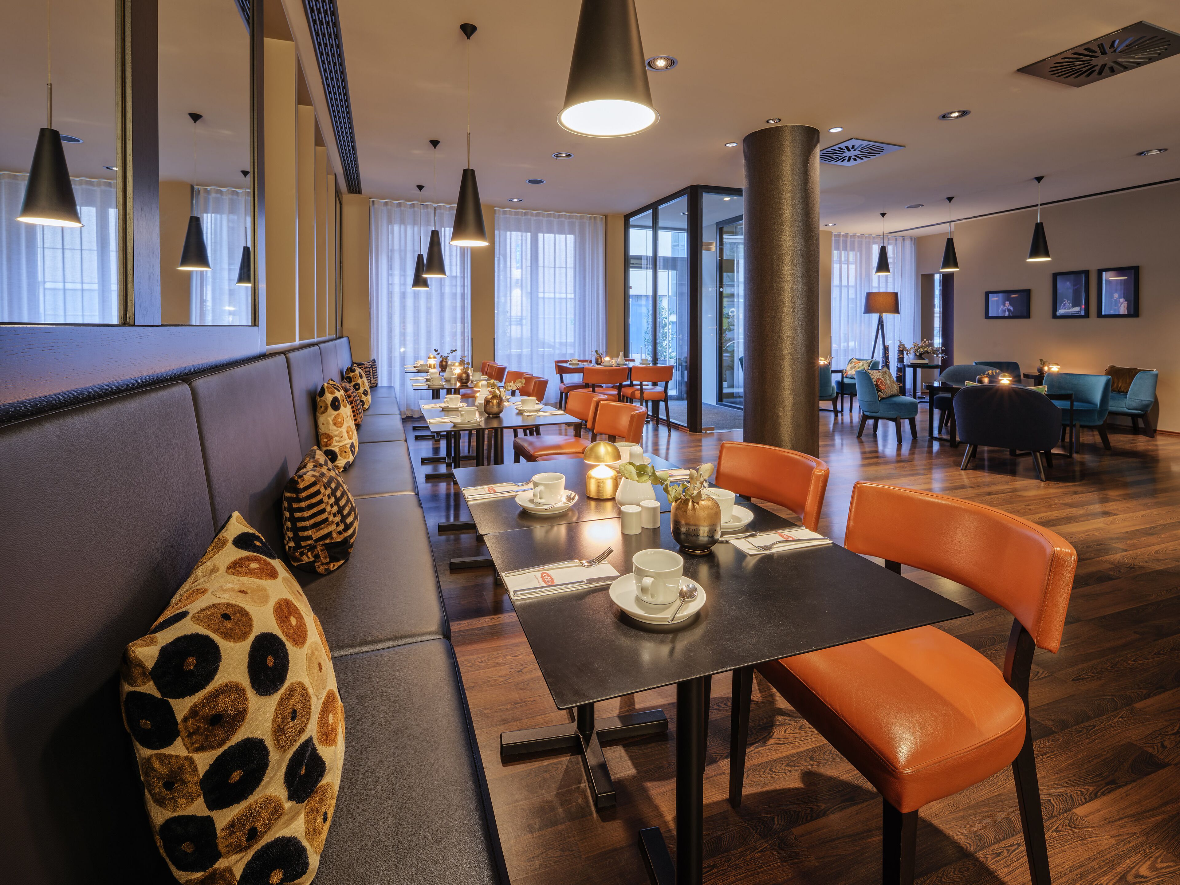 Un restaurant moderne avec des tables hautes, des chaises orange et un long banc agrémenté de coussins à motifs.