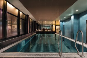 Piscina interior moderna com águas cristalinas, rodeada por paredes de vidro e grades de metal.