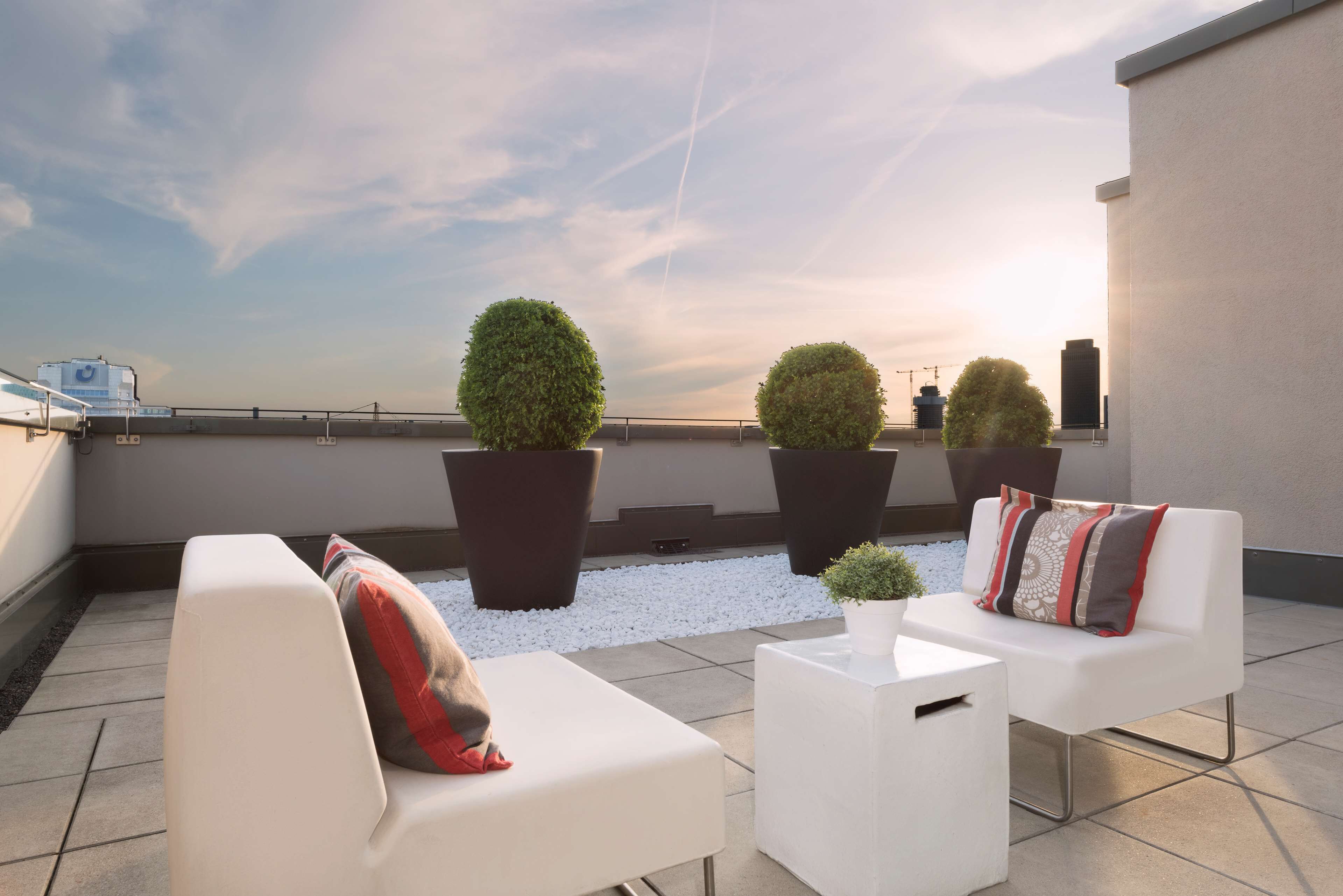 A rooftop terrace with white sofas, potted plants, and a clear view of the sky.