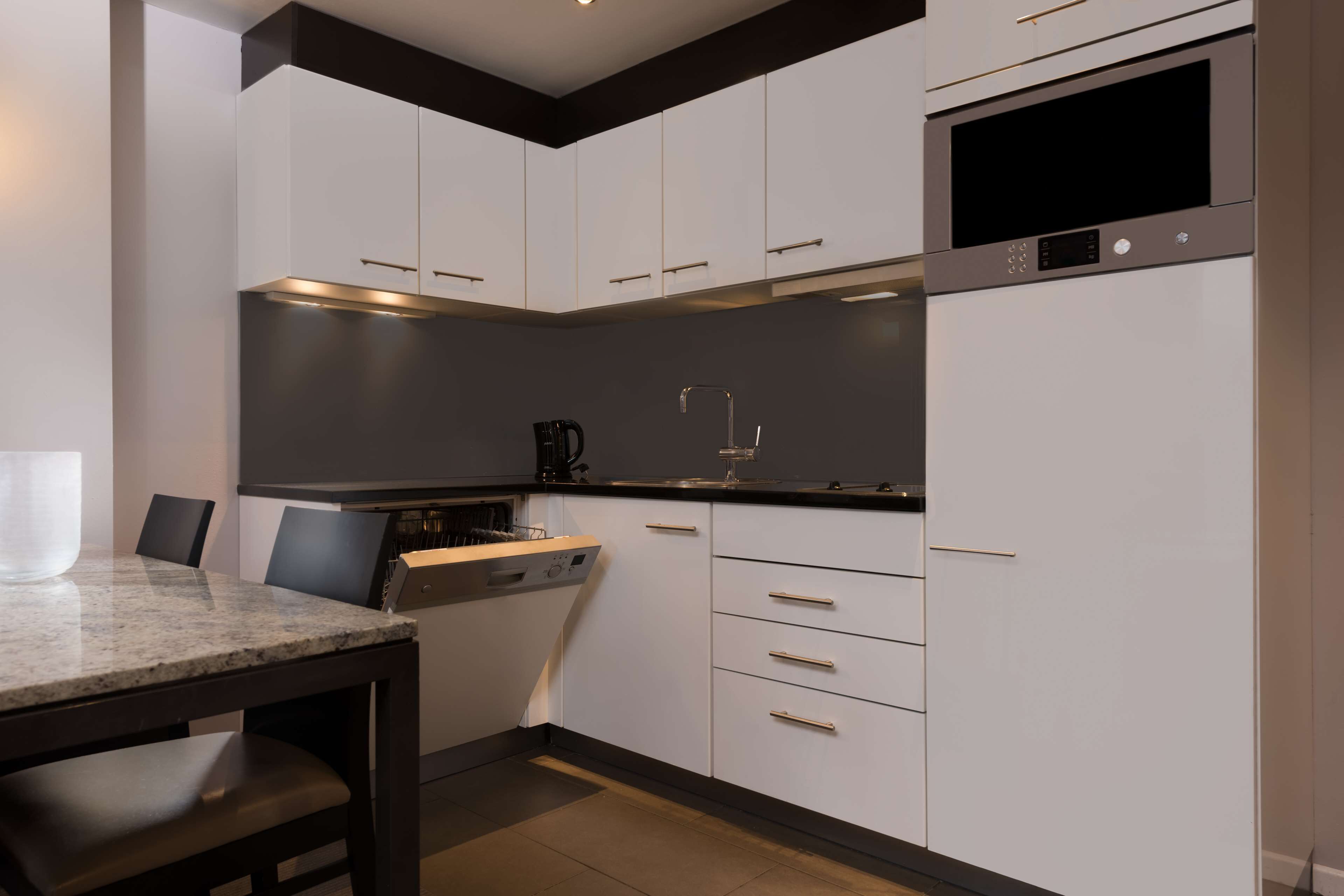 Una cocina moderna con armarios blancos, encimera negra y microondas integrado.