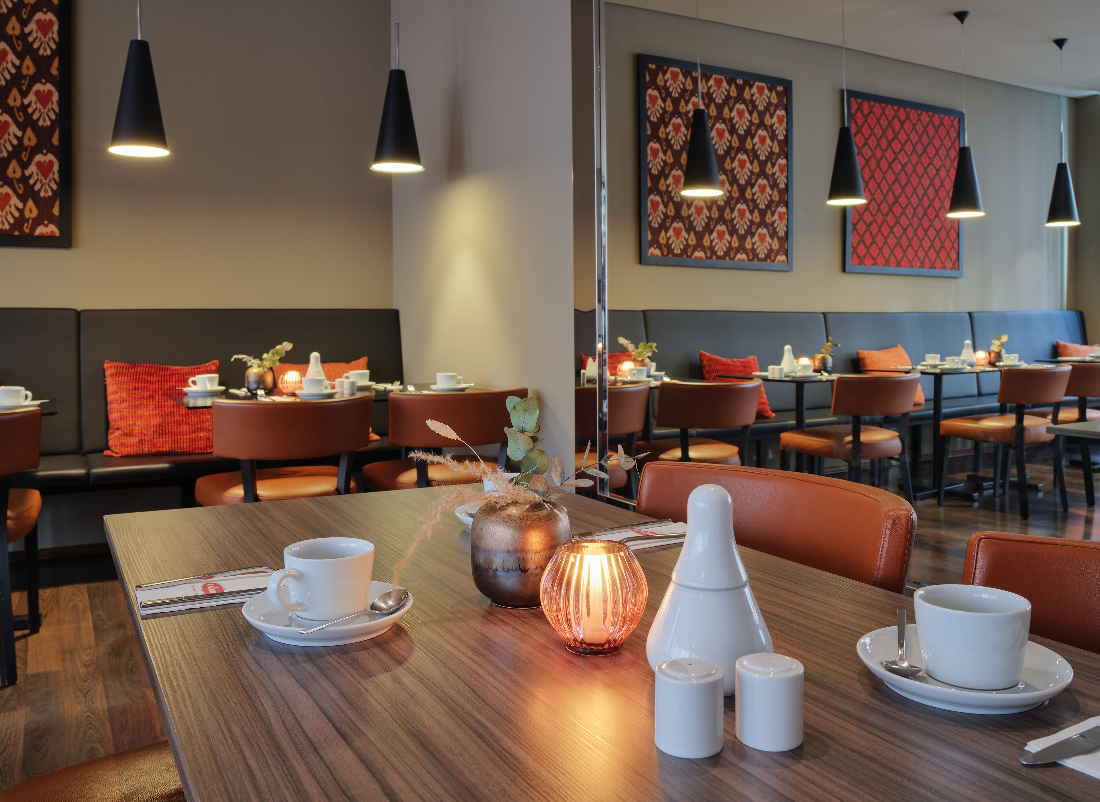 A restaurant with wooden tables, orange chairs, and black pendant lights.