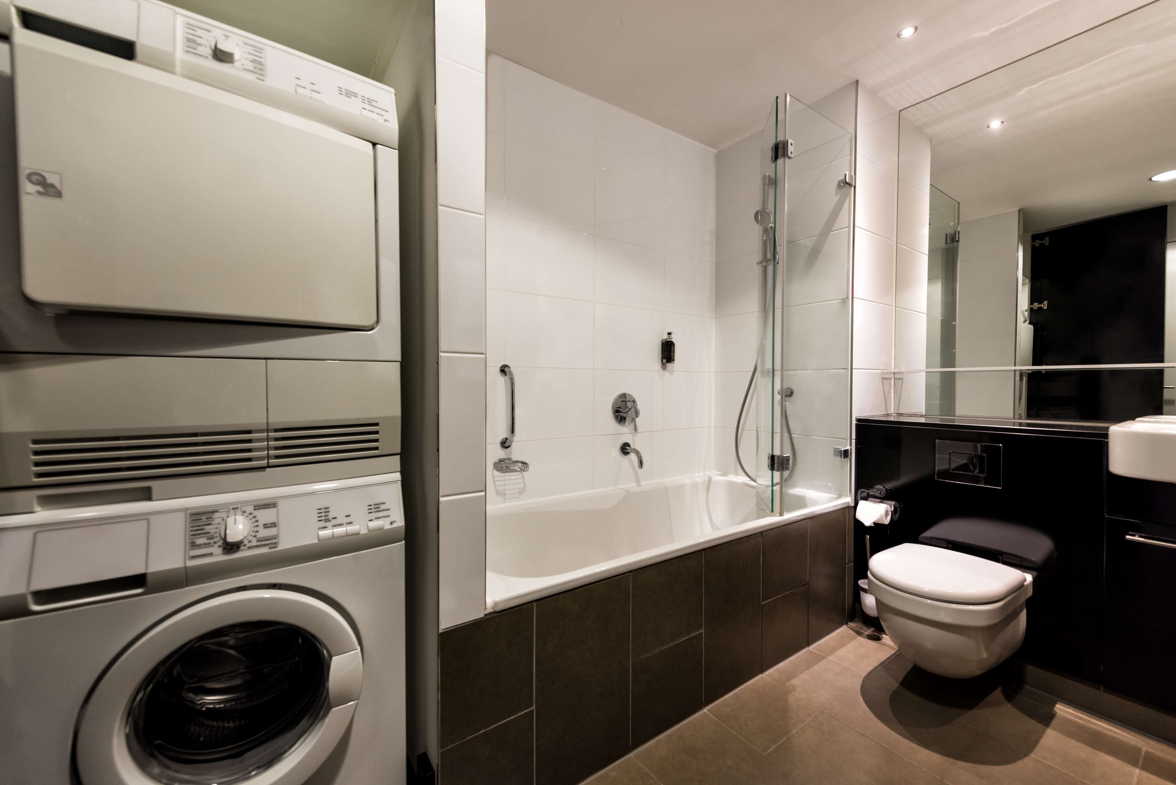 A modern bathroom with a washing machine, a bathtub, and a toilet.