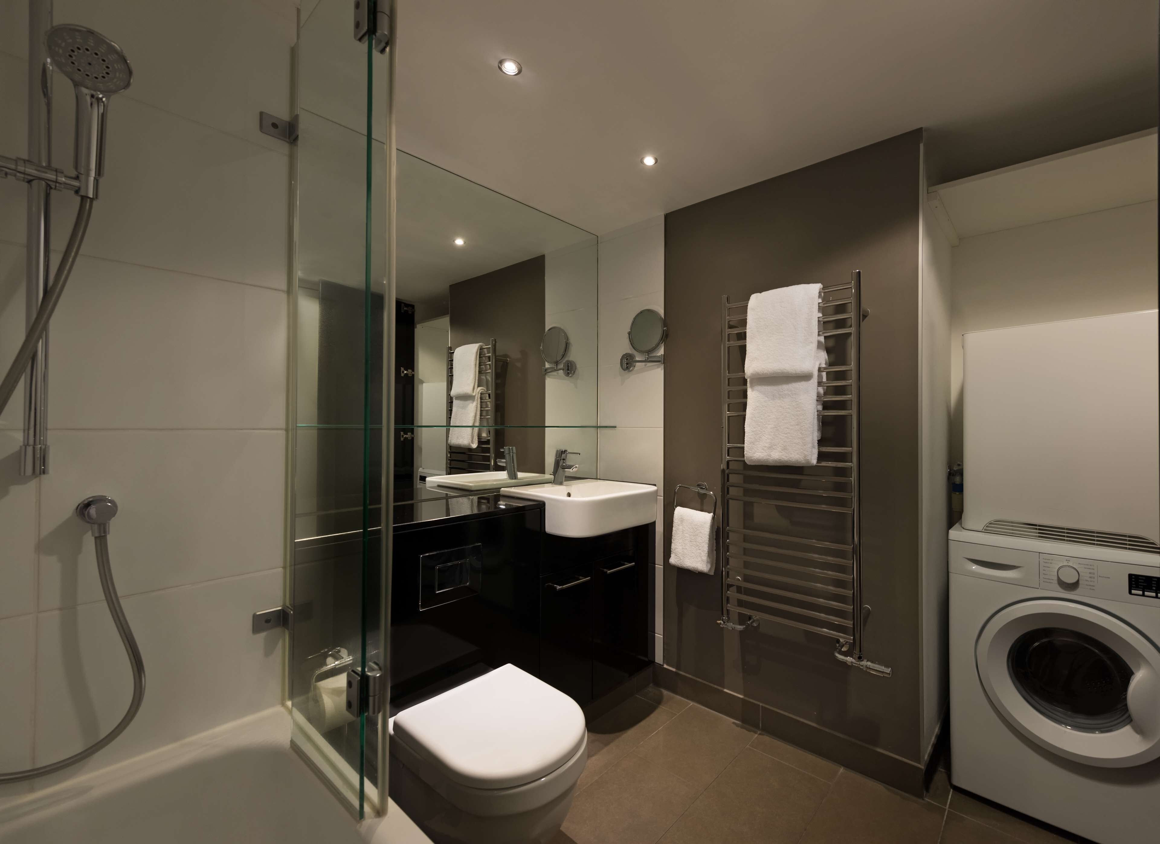 A modern bathroom with a glass-enclosed shower, a toilet, a sink, a mirror, and a built-in washing machine.