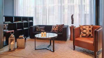 Ein modernes Wohnzimmer mit Sofa, Sessel und Couchtisch. Ein Bücherregal beherbergt Bücher und Dekorationselemente.
