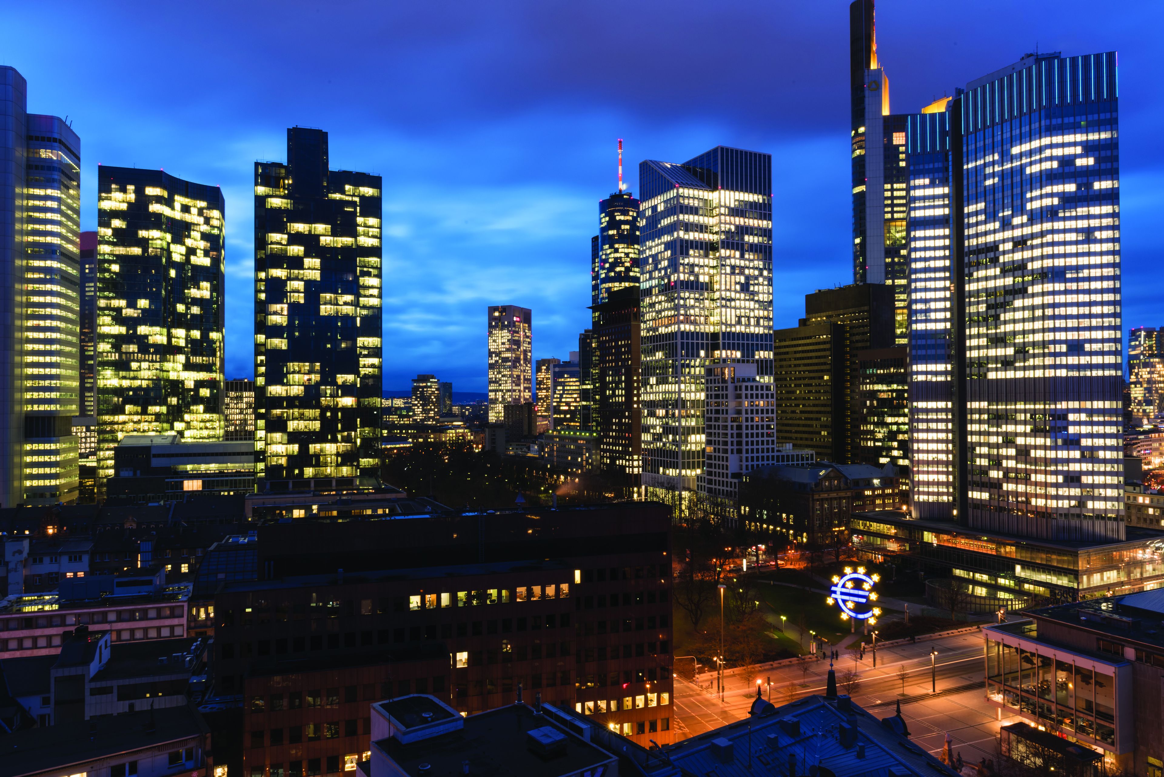 A cityscape at night with illuminated skyscrapers and a prominent circular light structure in the foreground.