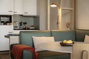 Una cocina moderna con armarios blancos, una zona de comedor con una mesa redonda y un sofá verde con un cuenco de limones.