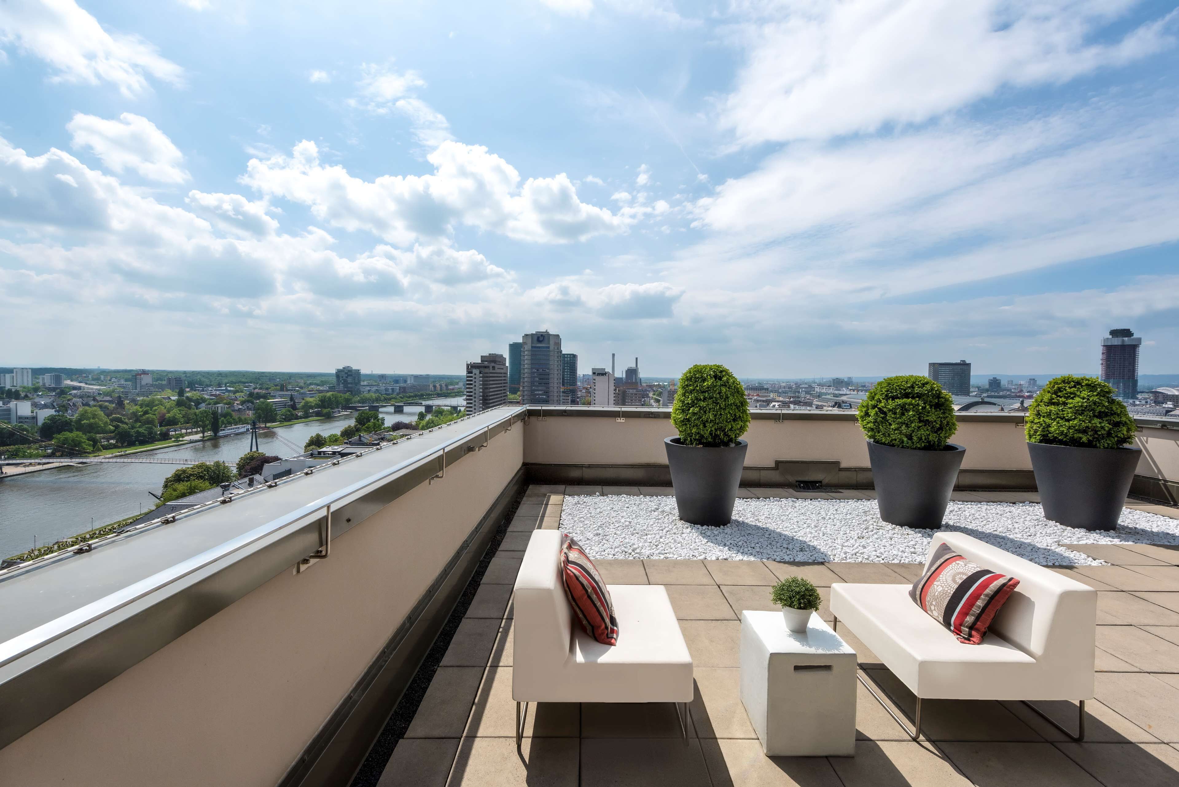 A rooftop terrace with a river view, white sofas, and potted plants.