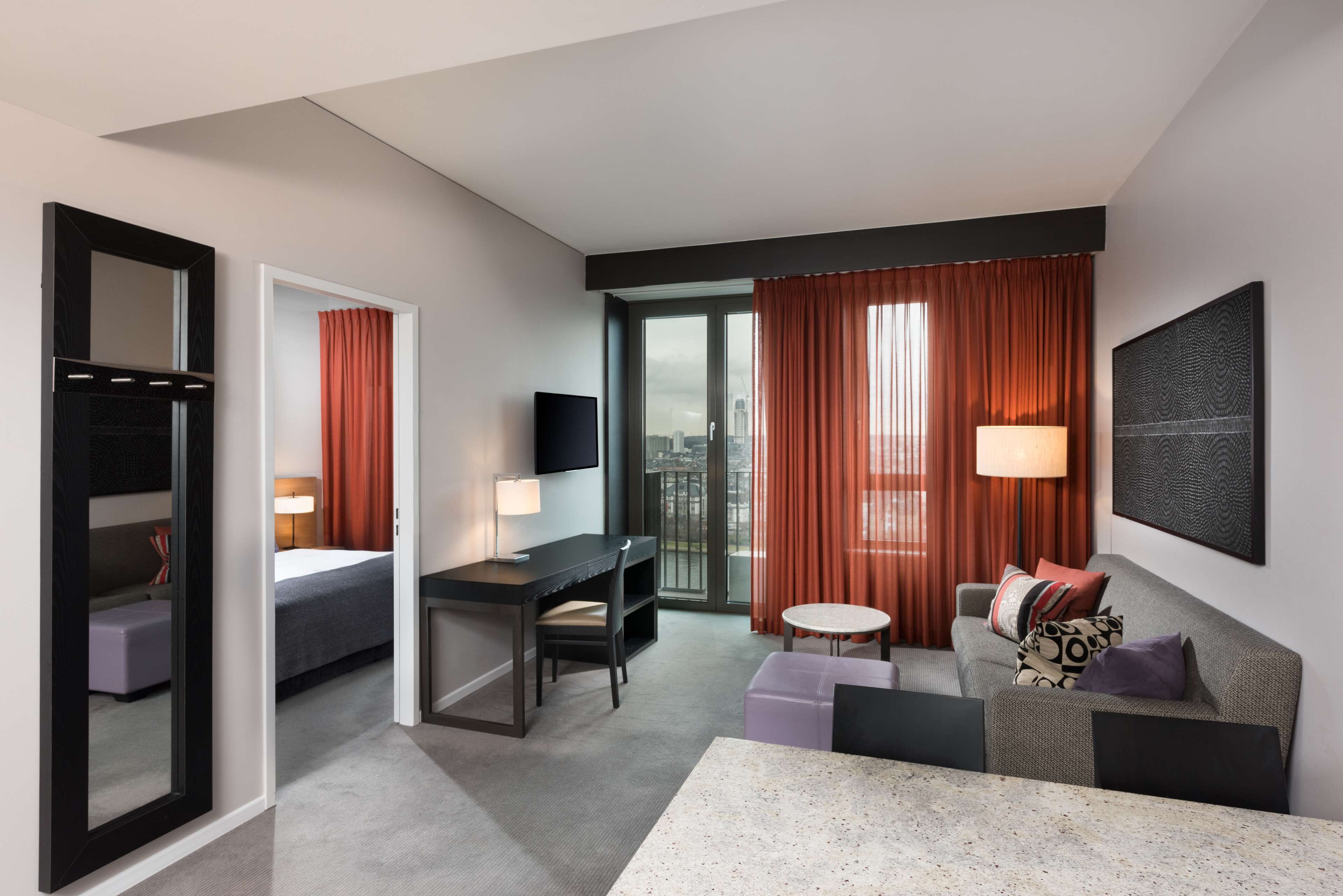 A modern hotel room with a bed, a desk, a sofa, and a TV.