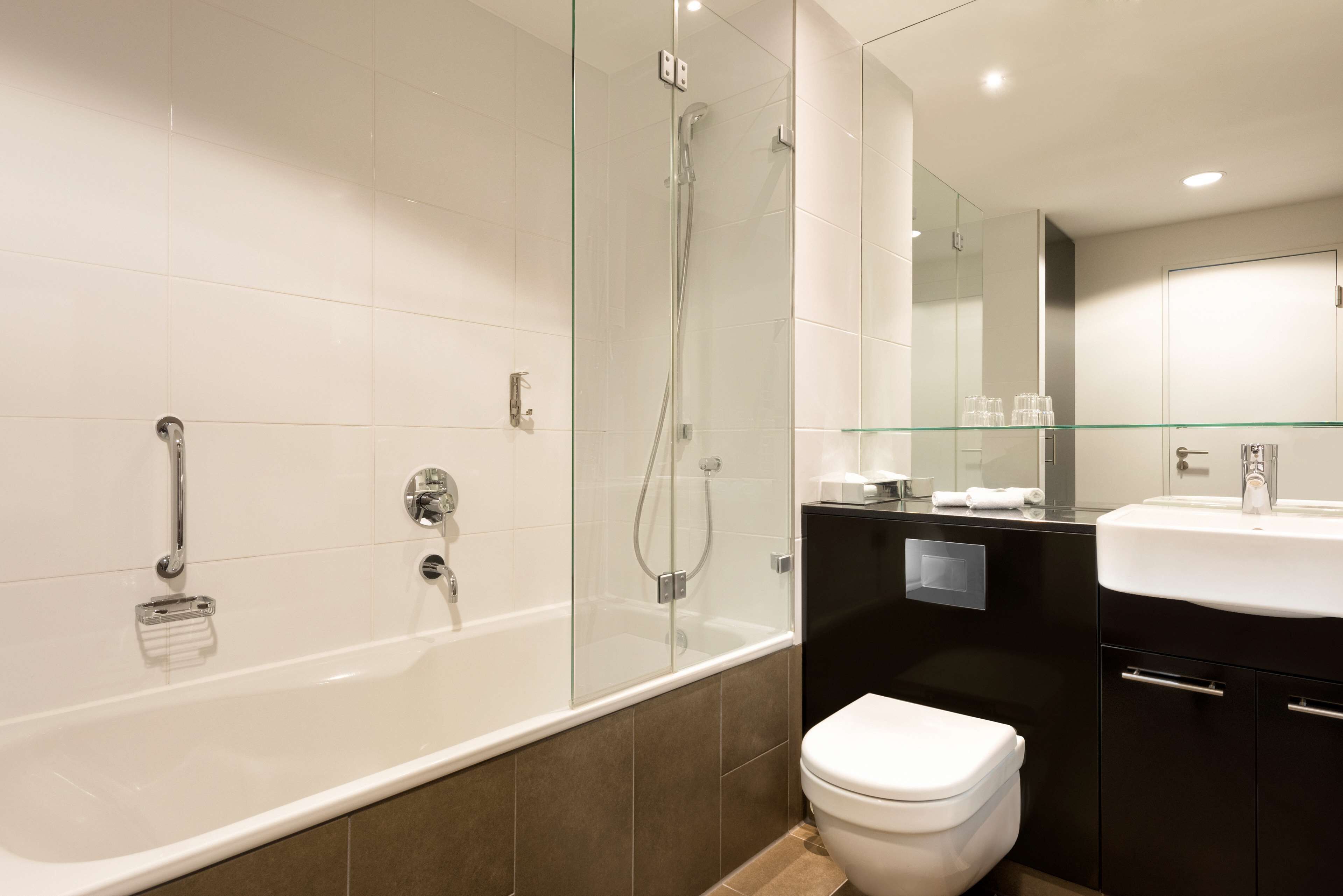 A modern bathroom with a glass-enclosed shower, a white bathtub, a toilet, and a vanity with a mirror.
