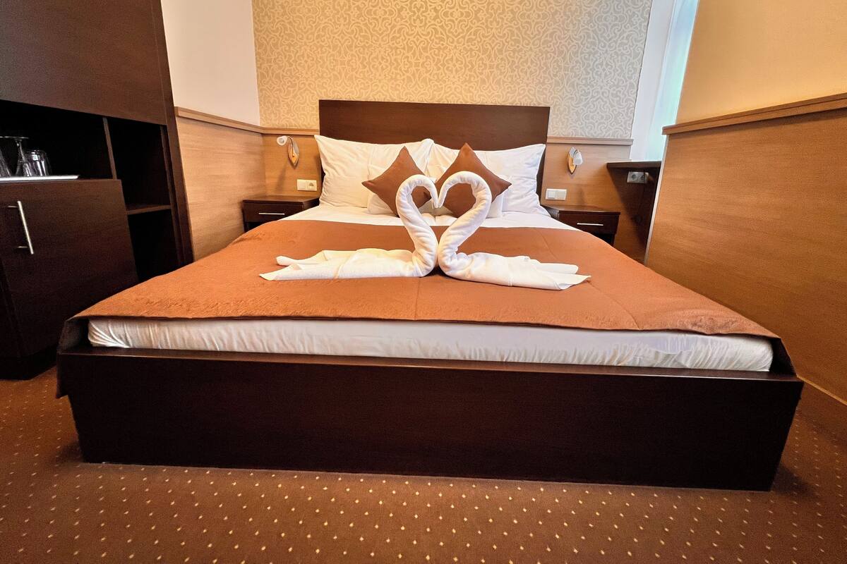 A hotel room with a large bed, a wooden headboard, a nightstand, a desk, and a wardrobe.