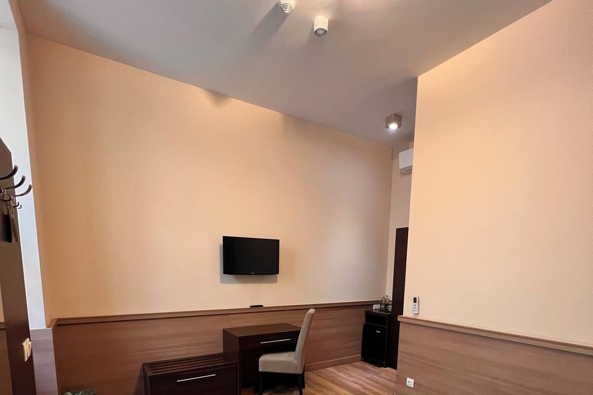 A modern hotel room with a large bed, a desk, a chair, a flat-screen TV, and a small trash bin.