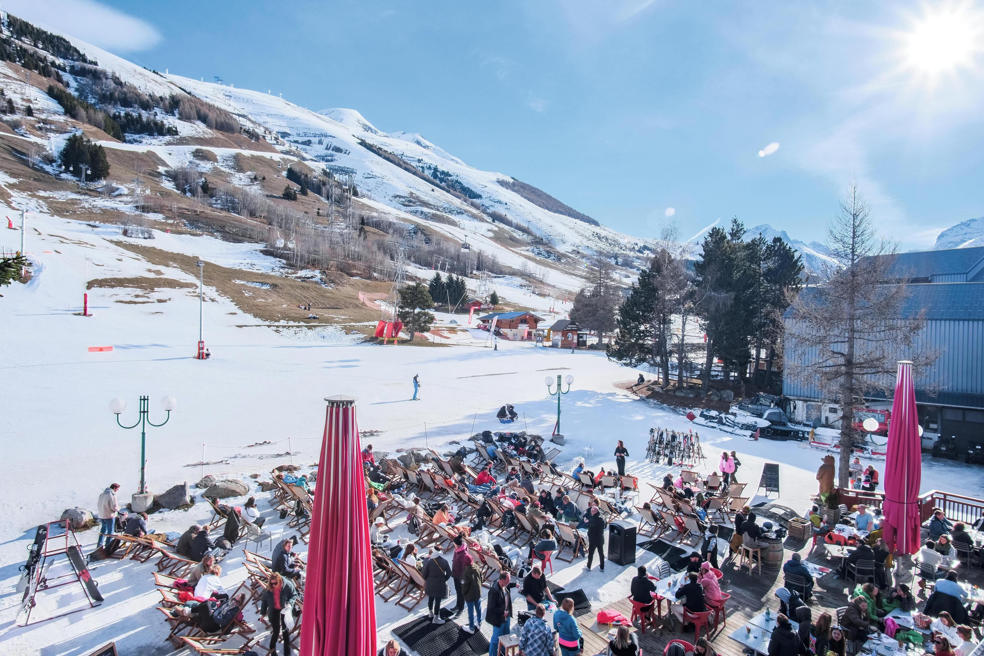 Een besneeuwde buitenruimte met tafels en stoelen, omgeven door met sneeuw bedekte heuvels en een heldere lucht.