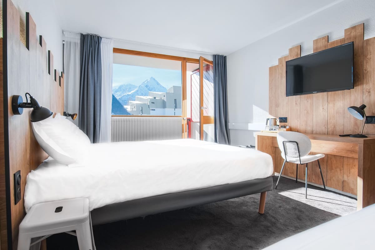 Une chambre d’hôtel avec un lit, un bureau, une chaise, une télévision et une vue sur les montagnes.