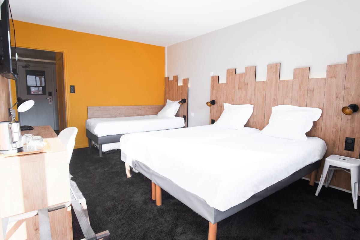 Une chambre d’hôtel avec deux lits, un bureau avec une chaise, un petit tabouret et un téléviseur.