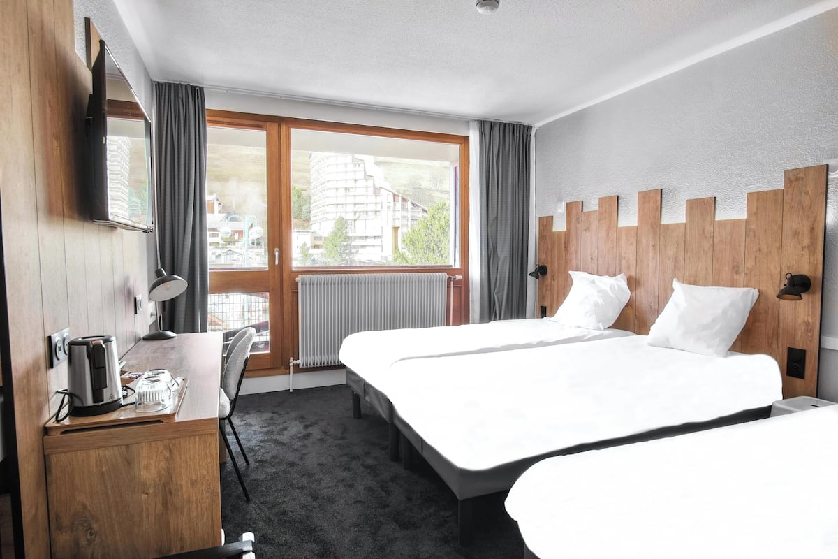 Une chambre d’hôtel avec deux lits, un bureau avec une bouilloire, une chaise, une télévision et une vue sur les bâtiments par la fenêtre.