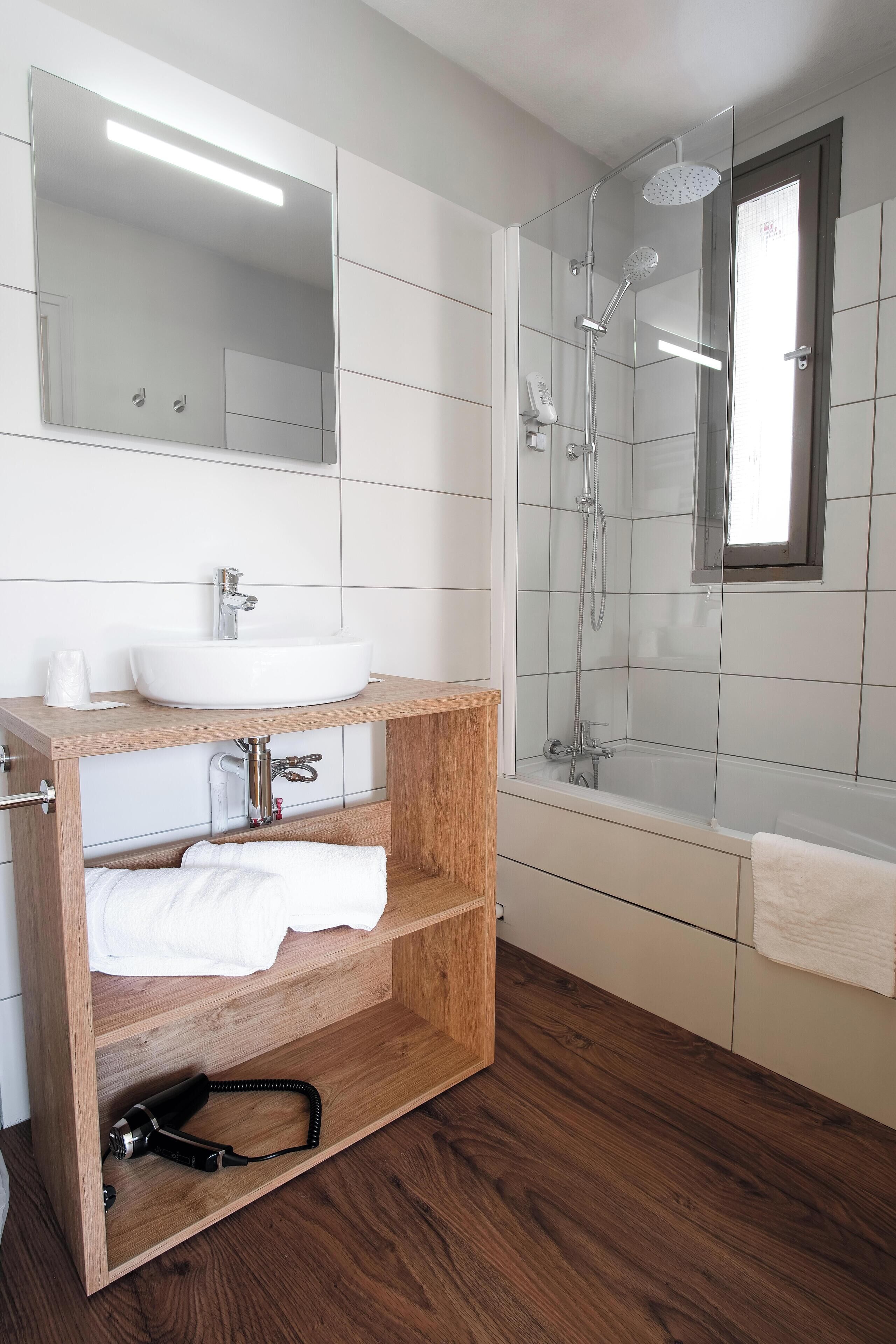 Een moderne badkamer met een witte wastafel, houten wastafelmeubel en douchecabine.