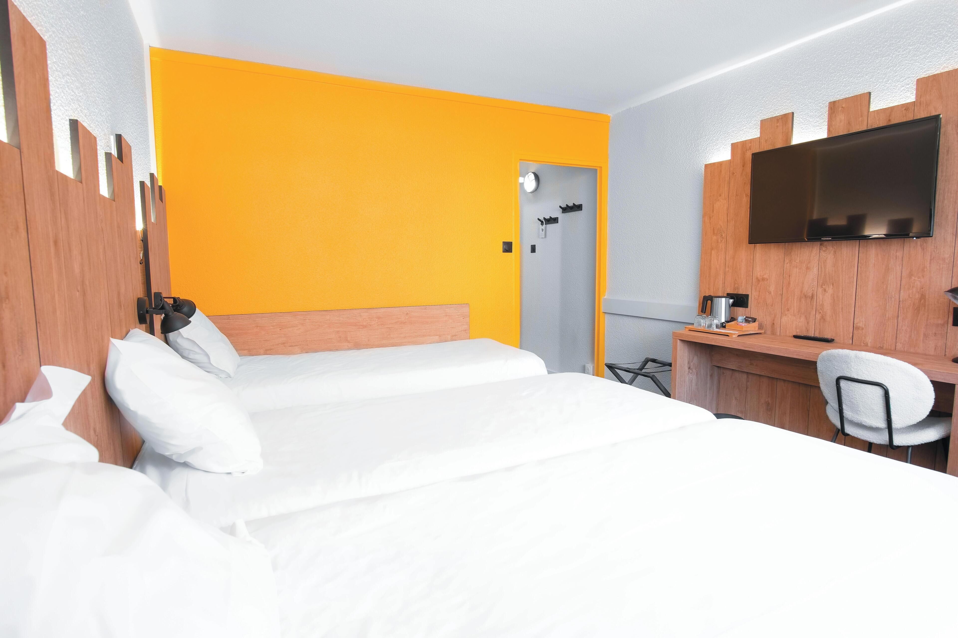 A hotel room with a bed, a desk, a chair, a TV, and a door.