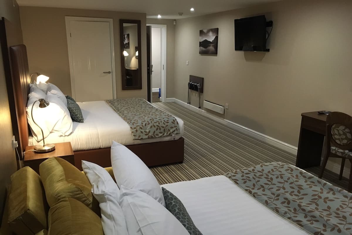 A hotel room with two beds, a sofa, a desk, a TV, and a mirror.