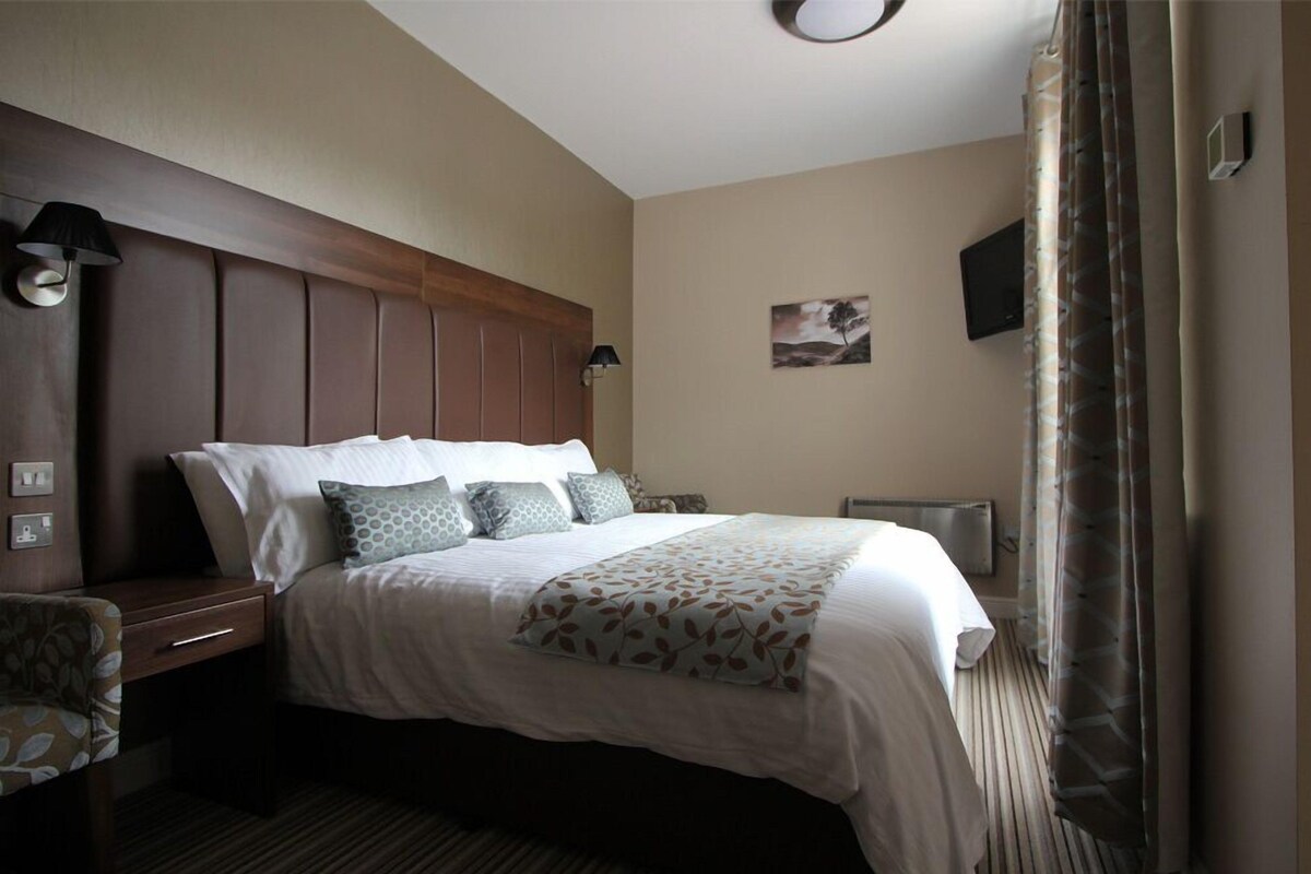 A hotel room with a large bed, bedside tables, a wall-mounted TV, and a painting.