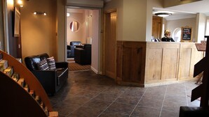 A reception area with a wooden counter, a black leather sofa, and a tiled floor. - Twin Oaks Hotel (Chesterfield)