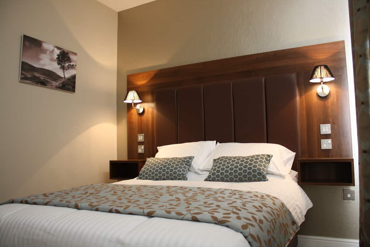 A neatly made bed with a patterned bedspread, a headboard with built-in lighting, and a wall-mounted flat-screen TV.