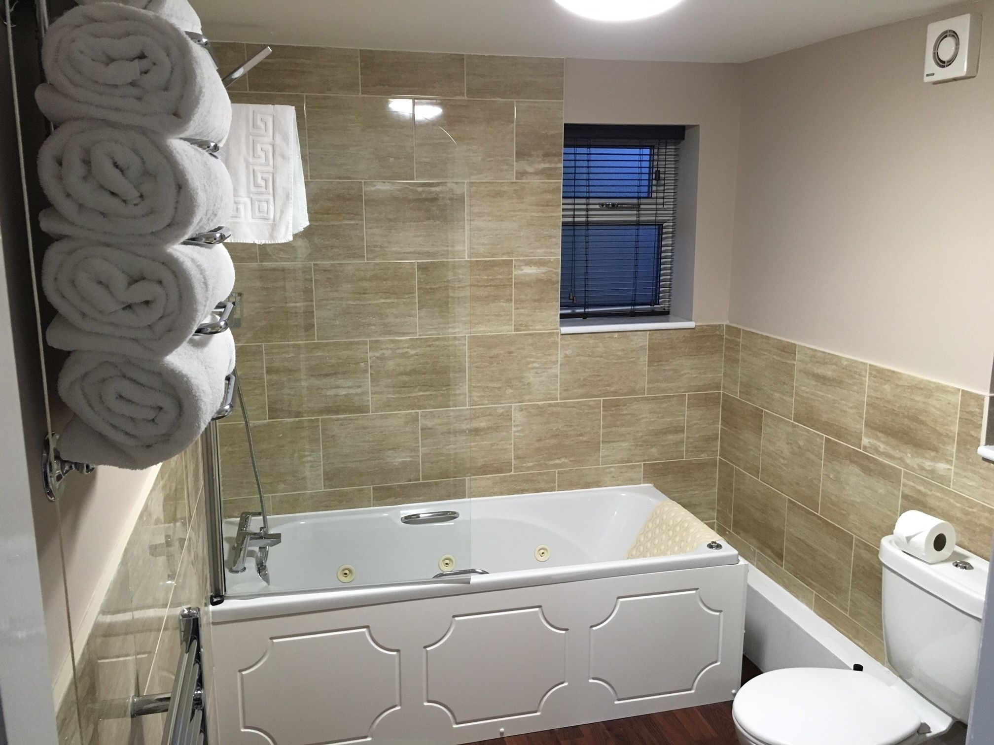 A bathroom with a bathtub, toilet, and a window with blinds.