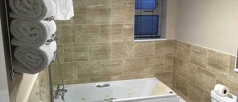 A bathroom with a bathtub, toilet, and a window with blinds.