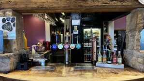 A bar area with a wooden counter, multiple beer taps, and a variety of bottles and glasses. - Twin Oaks Hotel (Chesterfield)