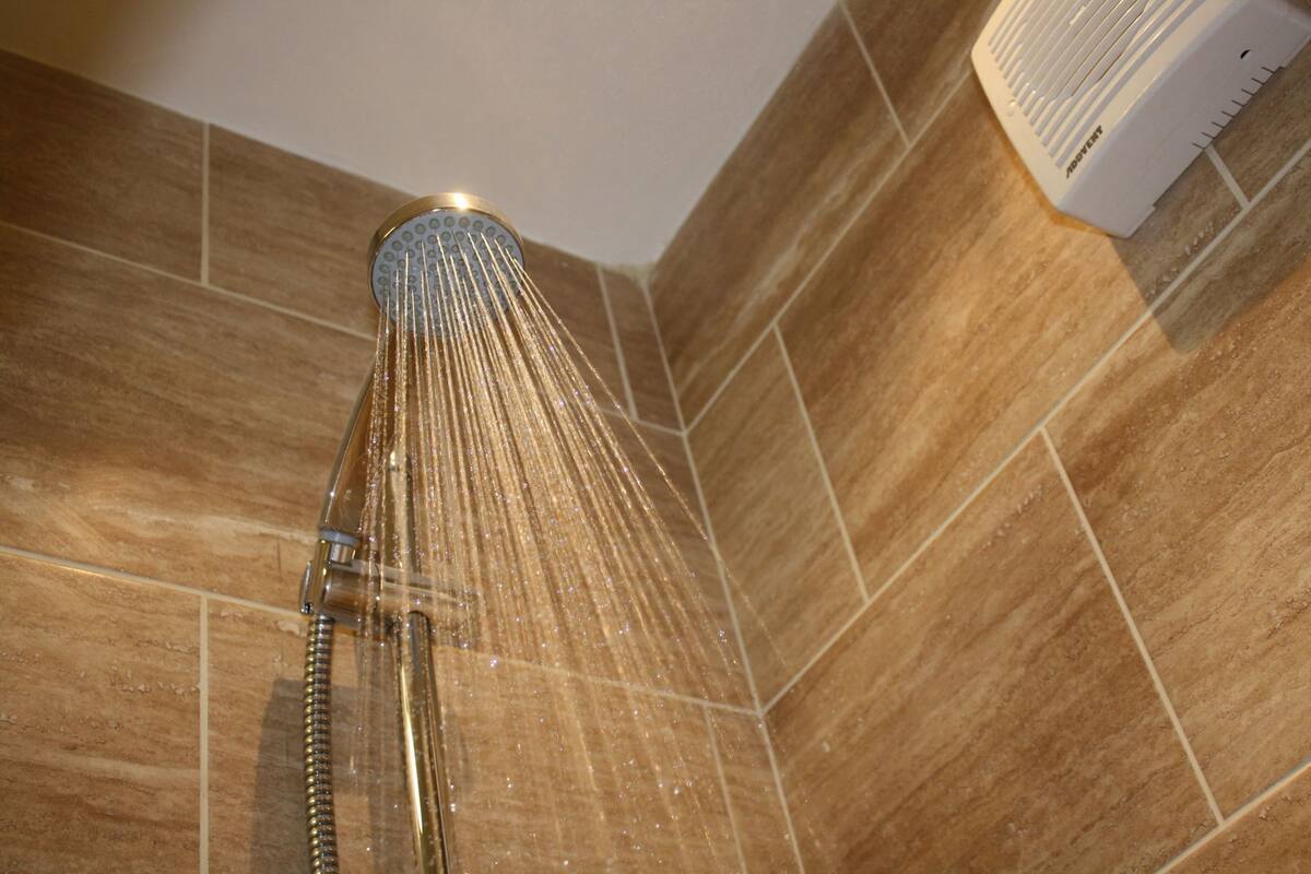 A showerhead with water flowing down, mounted on a tiled wall.