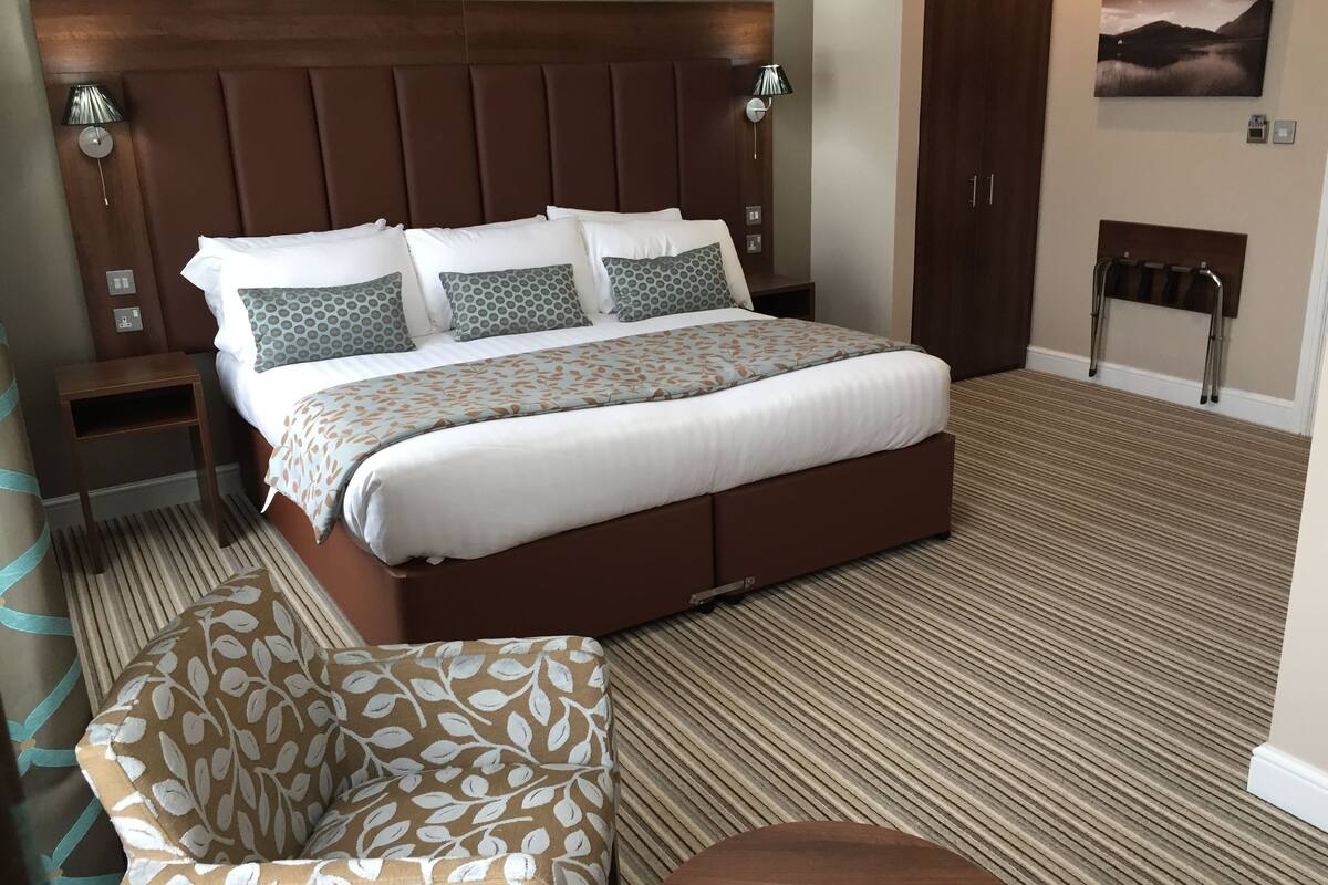 A neatly arranged bedroom with a large bed, a bedside table, a chair, and a wardrobe.