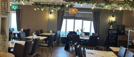 A restaurant with wooden tables and chairs, hanging lights, and a view of the street.