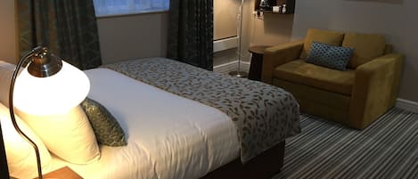 Een hotelkamer met een bed, een bedlamp, een sofa, een koffiezetapparaat en een televisie aan de muur.