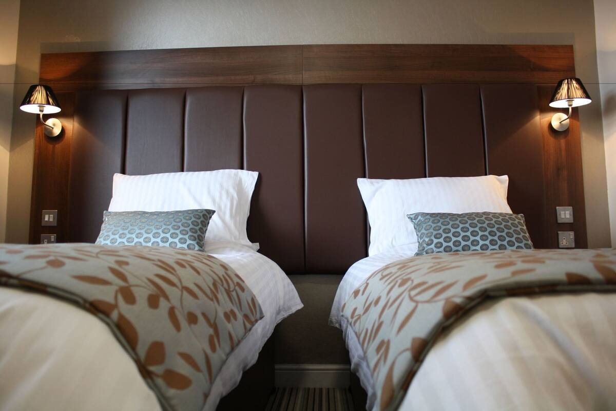 A hotel room with two beds, a wooden headboard, and wall-mounted lamps.