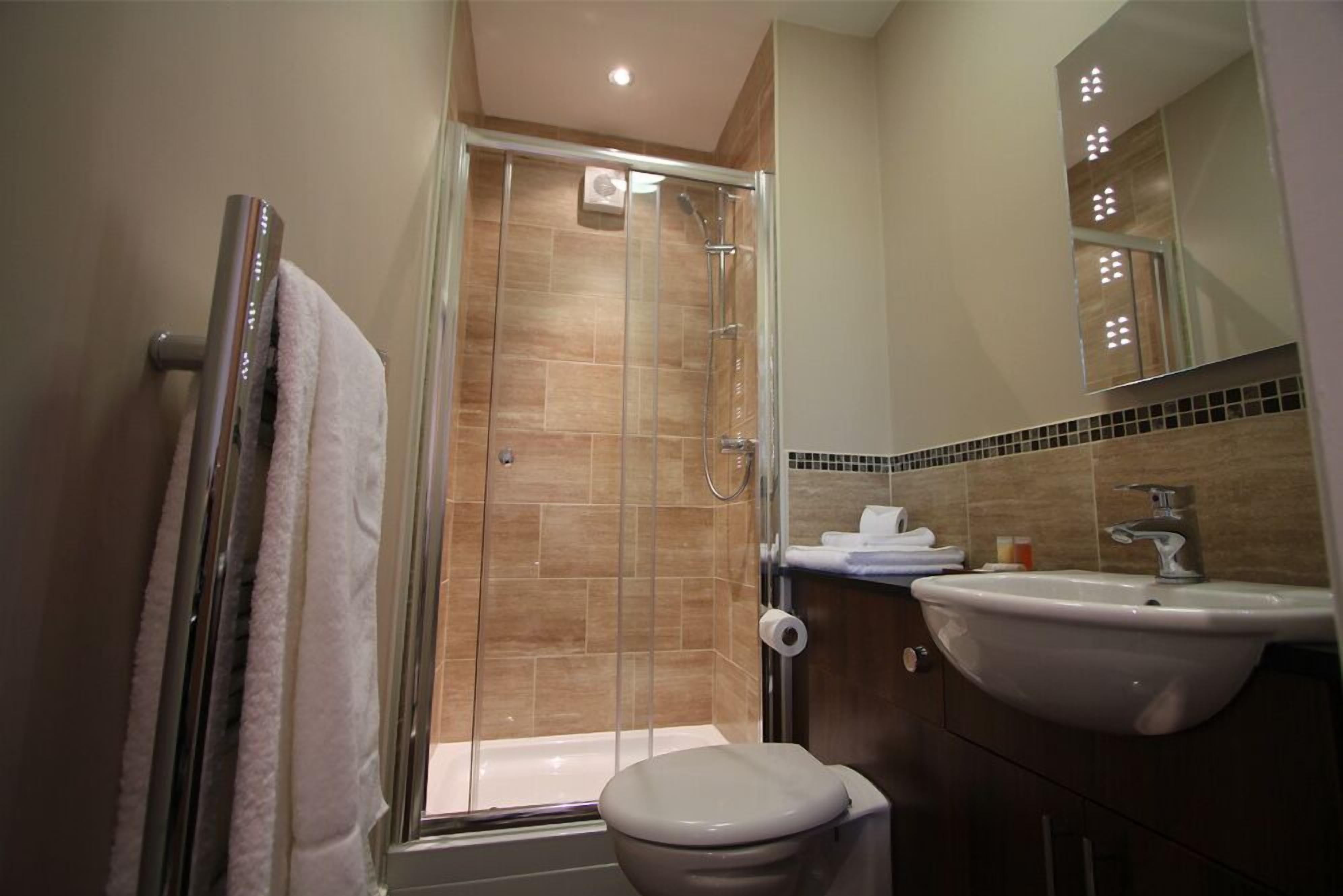 Une salle de bain moderne avec une douche à parois de verre, des toilettes blanches et un lavabo surmonté d’un miroir.