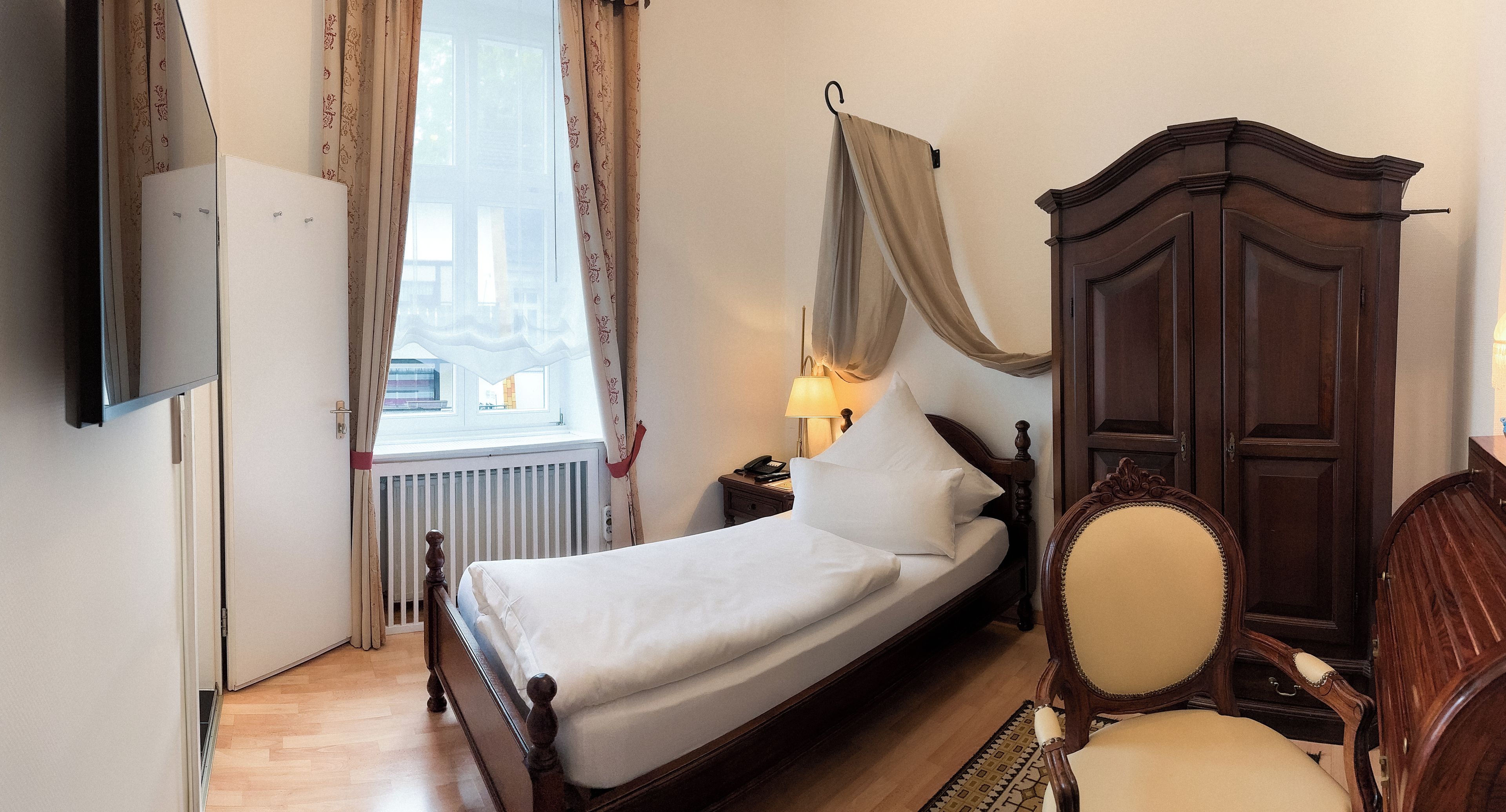 Una camera d'albergo con un letto, un comodino con una lampada, un armadio e una sedia.