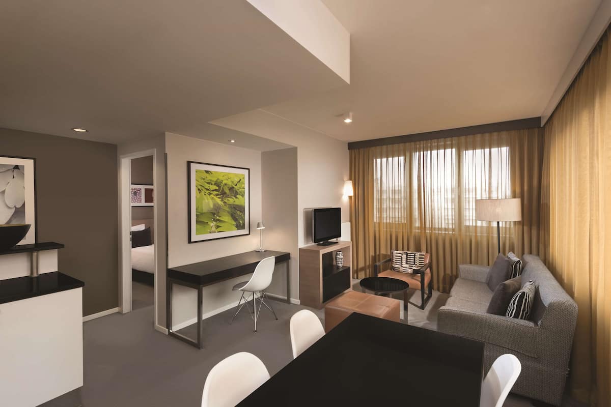 Ein modernes Hotelzimmer mit Essbereich, einer Couch, einem Fernseher und einem Schreibtisch.