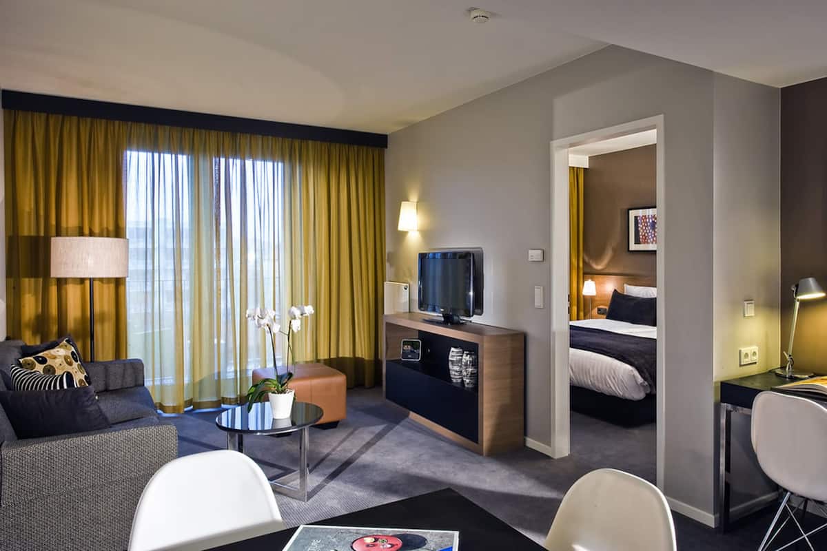 Ein modernes Hotelzimmer mit Sofa, Couchtisch, Fernseher, Bett und Schreibtisch.