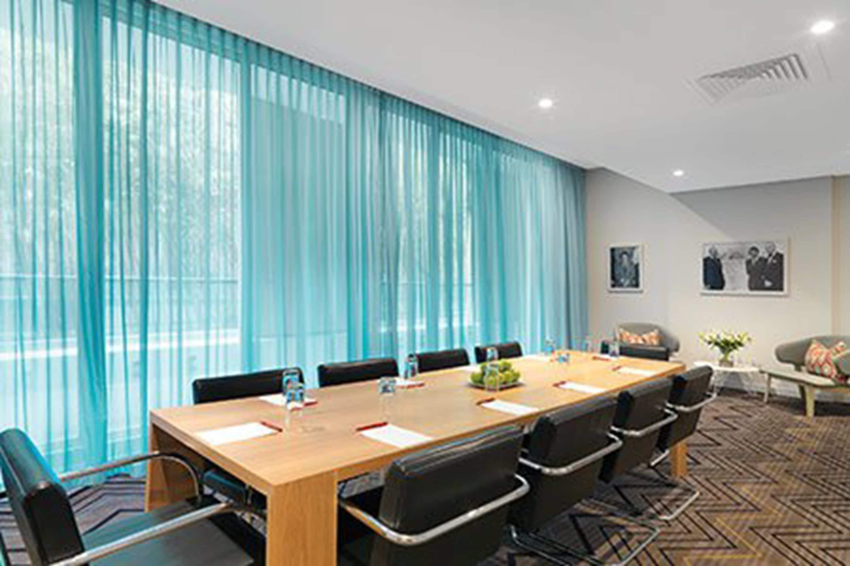 A conference room with a long table, chairs, and a large window with sheer curtains.