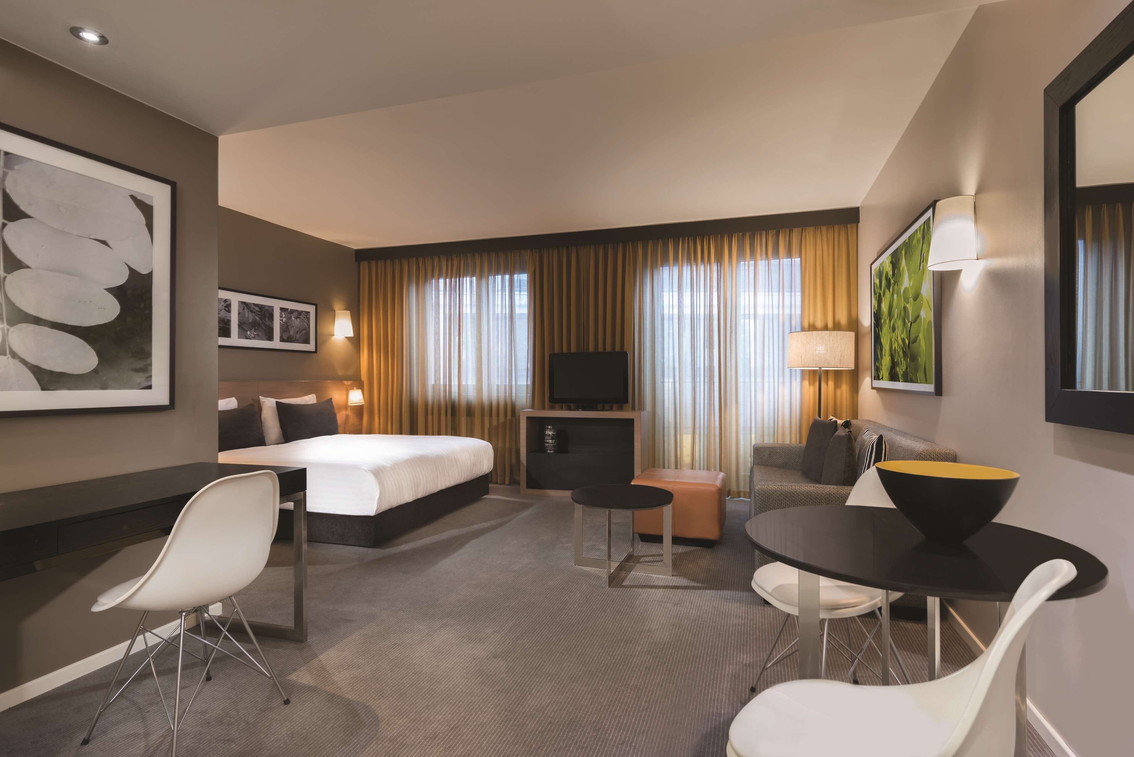 Habitación de hotel con cama, escritorio, silla, mesita, televisor y sofá.