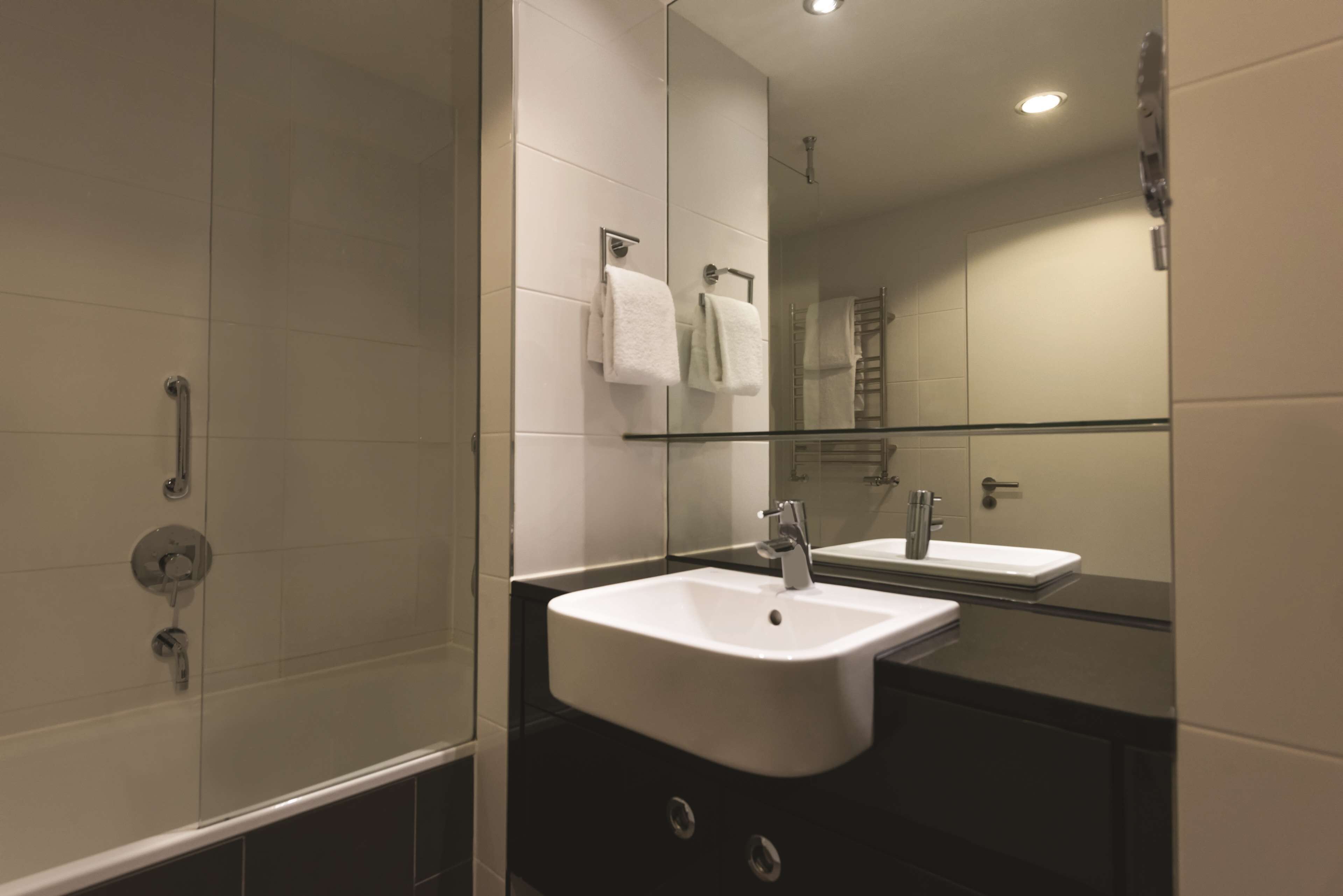 Une salle de bain moderne avec une douche à parois de verre, un lavabo blanc et un grand miroir.
